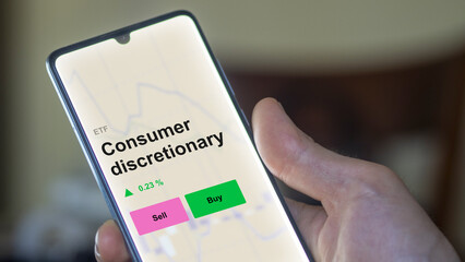 An investor's analizing the consumer discretionary etf fund on a screen. A phone shows the prices of Consumer discretionary