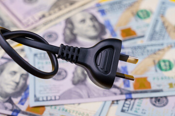 Plug from an electric cord tied in a knot on a blurred background of dollars, selective focus