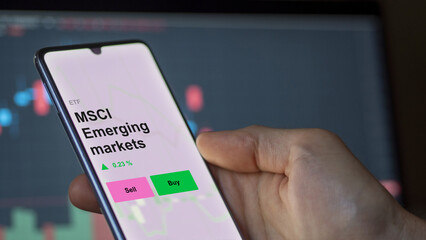 An investor's analizing the msci emerging markets etf fund on a screen. A phone shows the prices of MSCI Emerging markets