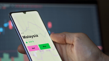 An investor's analizing the malaysia etf fund on a screen. A phone shows the prices of Malaysia