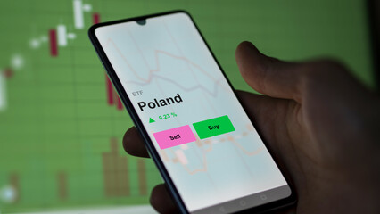 An investor's analizing the poland etf fund on a screen. A phone shows the prices of Poland
