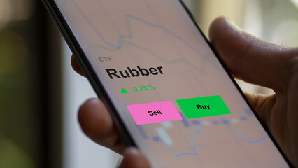 An investor's analizing the rubber etf fund on a screen. A phone shows the prices of Rubber