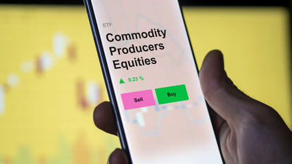 An investor analyzing the commodity producers equities etf fund on a screen. A phone shows the prices of commodities producers equity ETF.