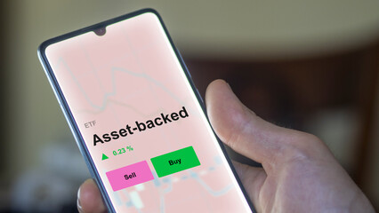 An investor's analizing the asset-backed etf fund on a screen. A phone shows the prices of asset backed