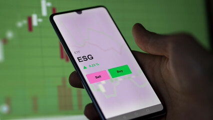 An investor's analizing the esg etf fund on a screen. A phone shows the prices of ESG