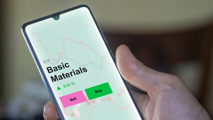 An investor's analizing the basic materials etf fund on a screen. A phone shows the prices of Basic Materials