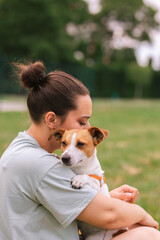 Woman in casual clothes hugging her favorite fluffy trained purebred Jack Russel Terrier dog outdoors in the nature on green grass meadow in summer day. Faithful best friends from childhood. Lifestyle