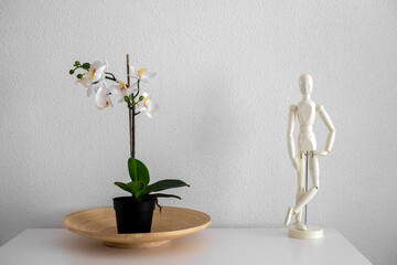 White wooden mannequin stands on the white table near white orchid. Home decoration elements