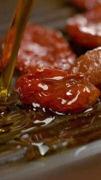 SLOW MOTION, MACRO, DOF: Healthy olive oil is being poured over the homegrown sun-dried tomatoes. Cured cherry tomatoes are heating up on the teflon grill pan as tasty olive oil splashes over them.