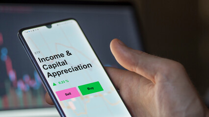 An investor's analizing the income & capital appreciation etf fund on a screen. A phone shows the prices of Income & Capital Appreciation