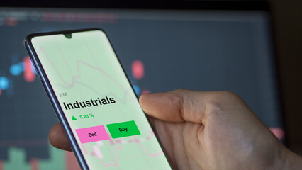 An investor's analizing the industrials etf fund on a screen. A phone shows the prices of Industrials