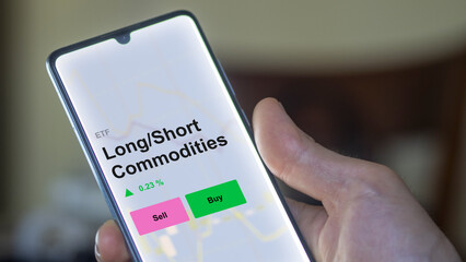 An investor's analizing the long/short commodities etf fund on a screen. A phone shows the prices of long / short Commodities