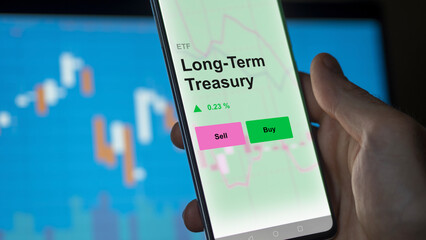 An investor's analizing the long-term treasury etf fund on a screen. A phone shows the prices of long term Treasury