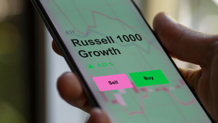 An investor's analizing the russell 1000 growth etf fund on a screen. A phone shows the prices of Russell 1000 Growth