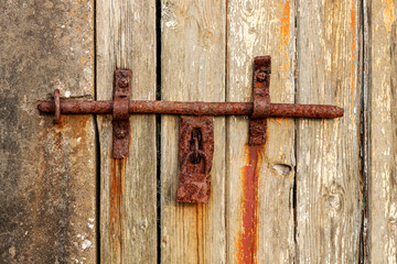 Fragment of an old wooden barn door background. There is a rusty forged bolt and closed lock. Texture.