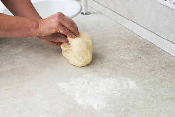 Woman cook kneads dough on modern kitchen table.