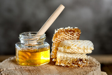 jar of honey with honeycomb and a dipper on  wooden stump.