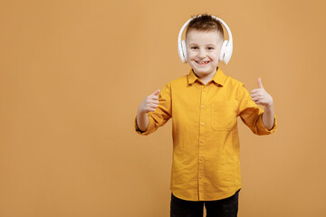 Portrait of funny clever school boy with headphones in yellow shirt. Yellow studio background. Education. Looking, smiling and shows a thumb up at camera. High quality photo