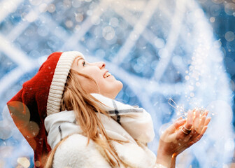happy woman in winter clothes holding Christmas light and smiling on cold winter snowing day