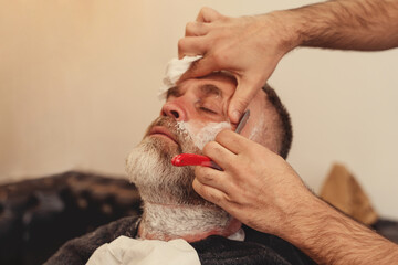 Shaving with a straight razor in a barbershop. A bearded old man being shaved in a barbershop....