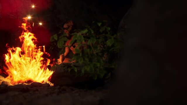 Dolly shot of an ancient hominid, neanderthal, homo sapiens in 3D sitting near a fire in a cave during Paleolithic age