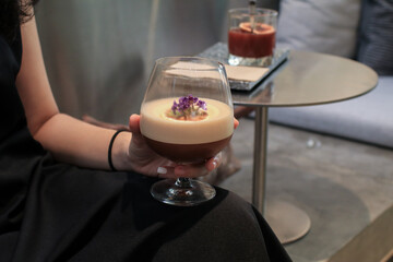Woman hand holding Espresso mocktail in wine glass based on coffee and juice on wood background. Creative new exotic cocktail drinks a combination of cold brew coffee with juice.