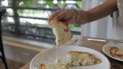 Chica joven toma porción de pizza vegana con verduras y salsa pesto en mesa blanca. Pizza sin...