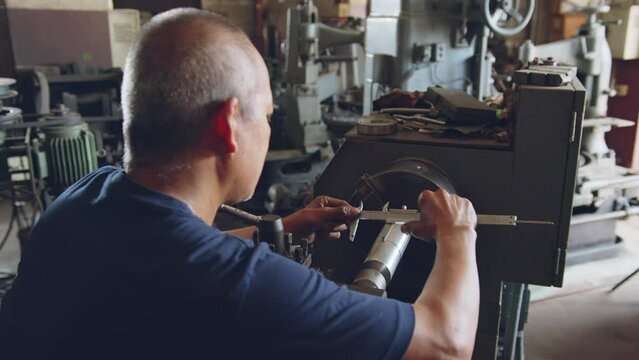 Technician asia worker using vernier caliper measure detail of workpiece for checking size in workshop lathe machine factory
