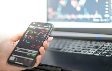 Female trader investor broker analyst holding a smartphone in hand analyzing stock market trading charts indexes data checking price using mobile
