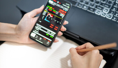 Female trader investor broker analyst holding a smartphone in hand analyzing stock market trading charts