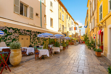 A picturesque alley of shops and sidewalk cafes in the colorful old town section of the Mediterranean resort city of Saint-Tropez, France, along the French Riviera.
