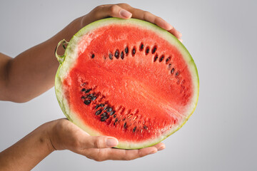 Half of watermelon in hands of unknown caucasian woman holding it in front of white wall background...