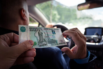 Passengers pay service fees to male taxi drivers. client pays for trip in rubles . 1000 rubles bill in a male hand