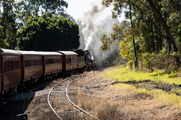 Fototapeta na wymiar Historic Mary Valley Rattler steam engine with vintage carriages rounding a curve on the line at Gympie, Queensland.