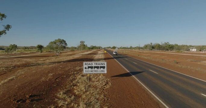 Road train sign alongside a straight road stretching through the Australian outback.