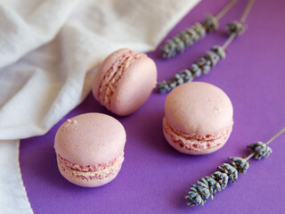 three pink pastel macaroons close-up on bright purple background with lavender flower and white cloth, Delicious strawberry raspberry cookies. Top view flat lay