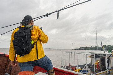 Latin fisherman with raincoat checking the weather forecast on his cell phone on top of his boat in...