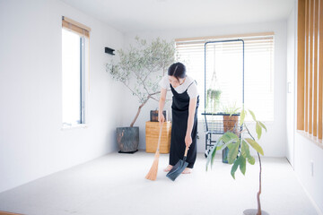 明るい植物の部屋でほうきで掃除する日本人女性