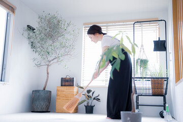 明るい植物の部屋でほうきで掃除する日本人女性