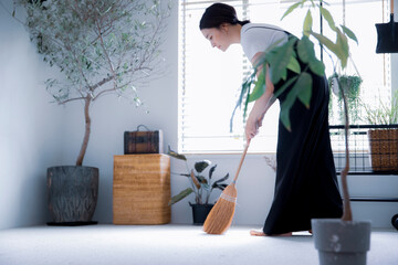明るい植物の部屋でほうきで掃除する日本人女性 - obrazy, fototapety, plakaty