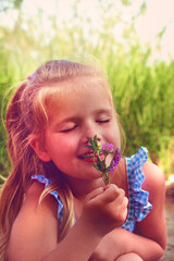 Little girl picking summer flowers in a field. Happy child enjoying nature outdoors. Sunlit  little girl smelling summer flowers