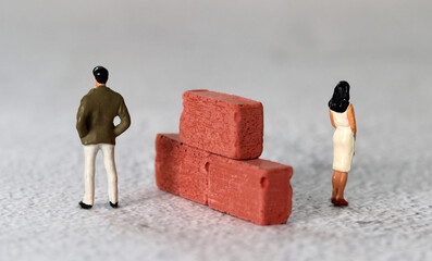 A miniature man and a miniature woman standing next to a brick. The concept of gender conflict.
