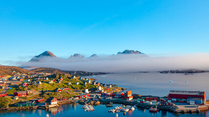 Naklejka premium A layer of fog spreads between the mountains and the sea -Picturesque village and Colorful houses on coast of Greenland - Tasiilaq, East Greenland