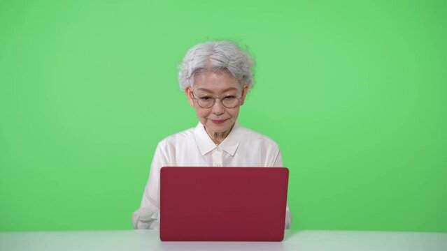 ノートパソコンを使うシニア女性　クロマキー合成用グリーンバック