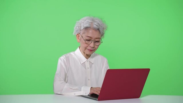 ノートパソコンを使うシニア女性　クロマキー合成用グリーンバック