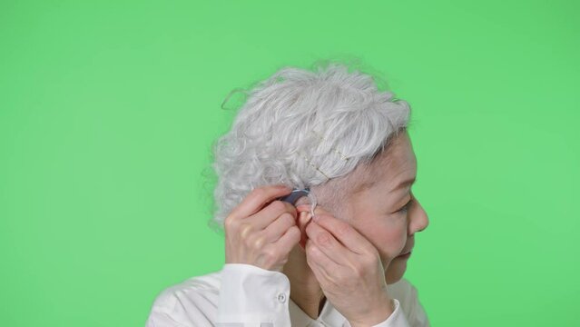 補聴器をつけるシニア女性　クロマキー合成用グリーンバック