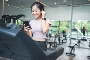 Fototapeta na wymiar Portrait of an Asian woman exercising on a treadmill She is listening to music with wireless headphones and a smart watch.
