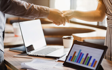 business men and women shaking hands at a meeting with graph and the laptop is placed on the business and commercial concept table.