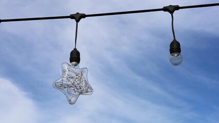 A star-shaped light bulb hung on the cable. A closeup of a retro-style clear glass bulb hanging on...