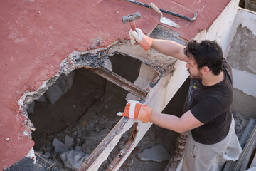 Young man pulling the roof of a house down using a mallet.